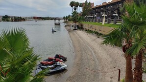 A beach with jet skis, a statue, and a building with a Western theme. - The New Pioneer (Laughlin)