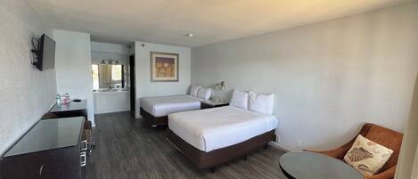 Habitación de hotel con dos camas, un escritorio, una silla, una mesita, un baño e iluminación en el techo.