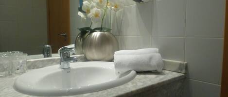 Un baño con lavamanos blanco, un espejo, toallero y un florero con flores.