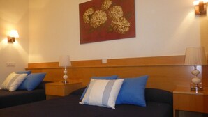 Habitación de hotel con dos camas, cada una con almohadas azules y blancas, y cabeceros de madera. Hay dos lámparas de noche y un cuadro en la pared.