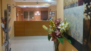Zona de recepción con un mostrador de madera, un jarrón de flores y un cartel en la pared.