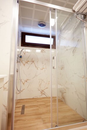 A glass-enclosed shower with a wooden floor and marble walls. - Mira Otel Alsancak (Izmir)