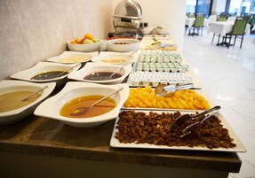 Un bufé con diferentes opciones de comida, incluyendo tazones de sopa, frutas y bandejas de pastelería.