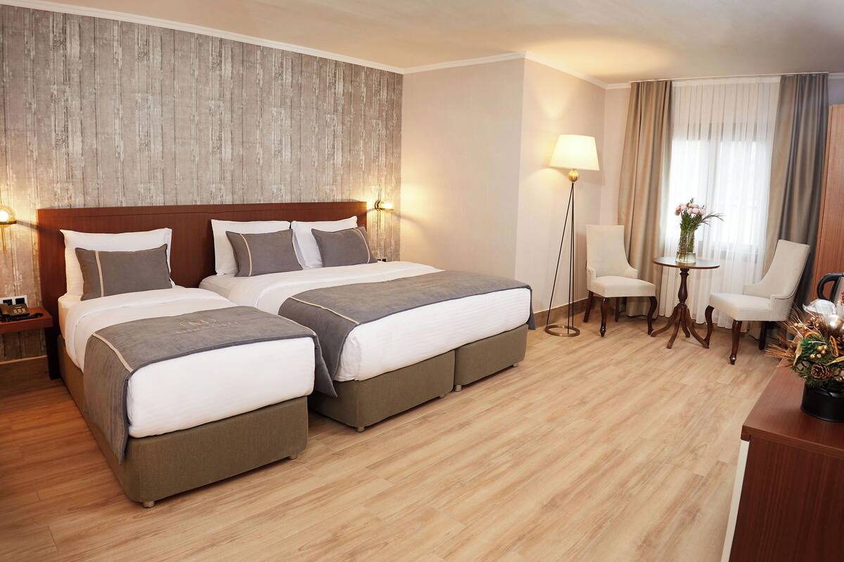 Hotelkamer met twee bedden, een bureau, een stoel, een lamp en een tafeltje met een vaas.