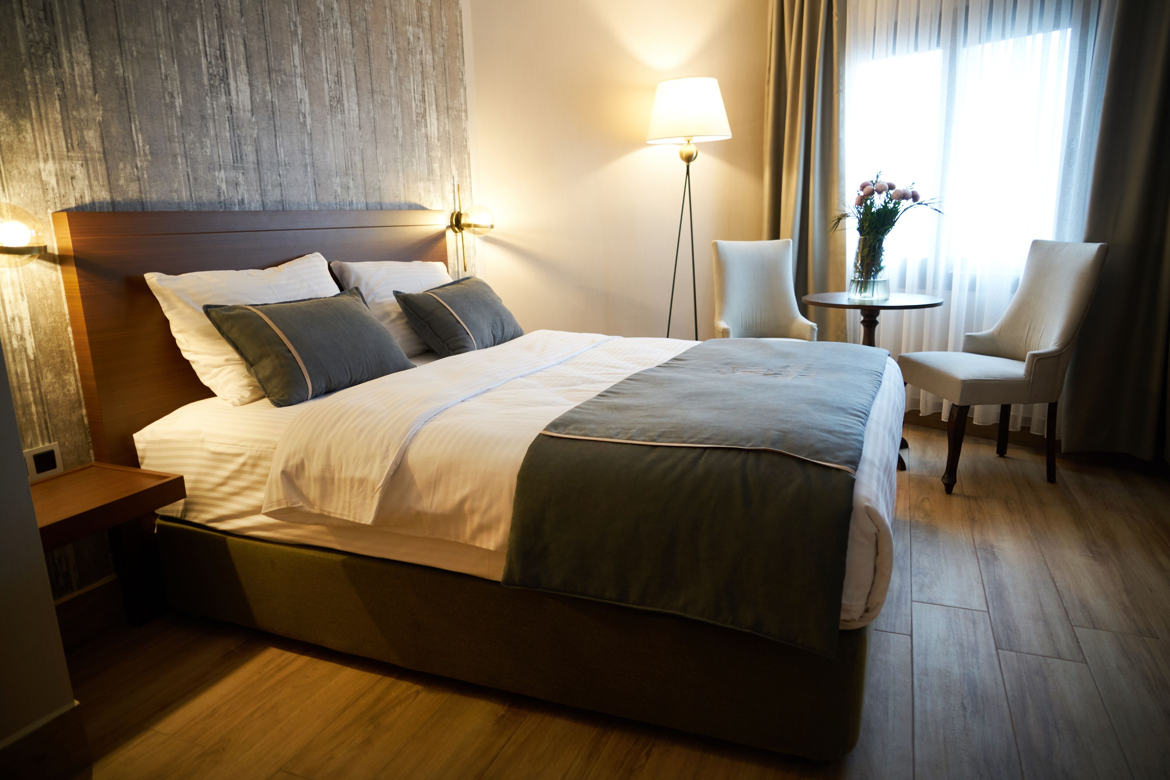 Hotellihuone, jossa on suuri sänky, yöpöydät, työpöytä, tuoli, lamppu ja ikkuna, jossa on verhot.