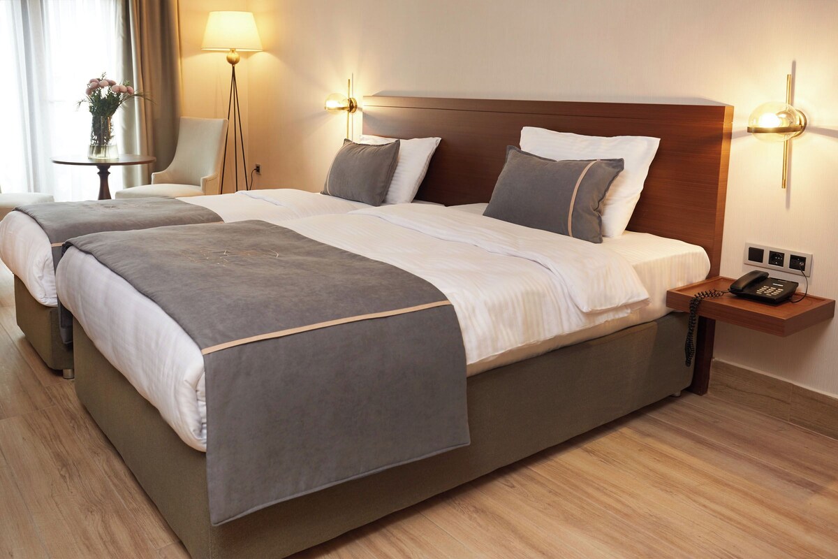 A hotel room with a large bed, bedside lamps, a nightstand with a phone, and a small table with a vase.
