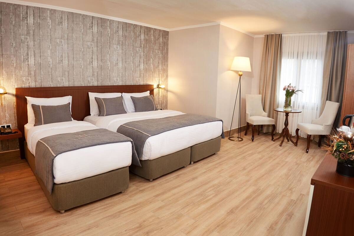 Een hotelkamer met twee bedden, een bureau, een stoel, een lamp en een kleine tafel met een bloevas.