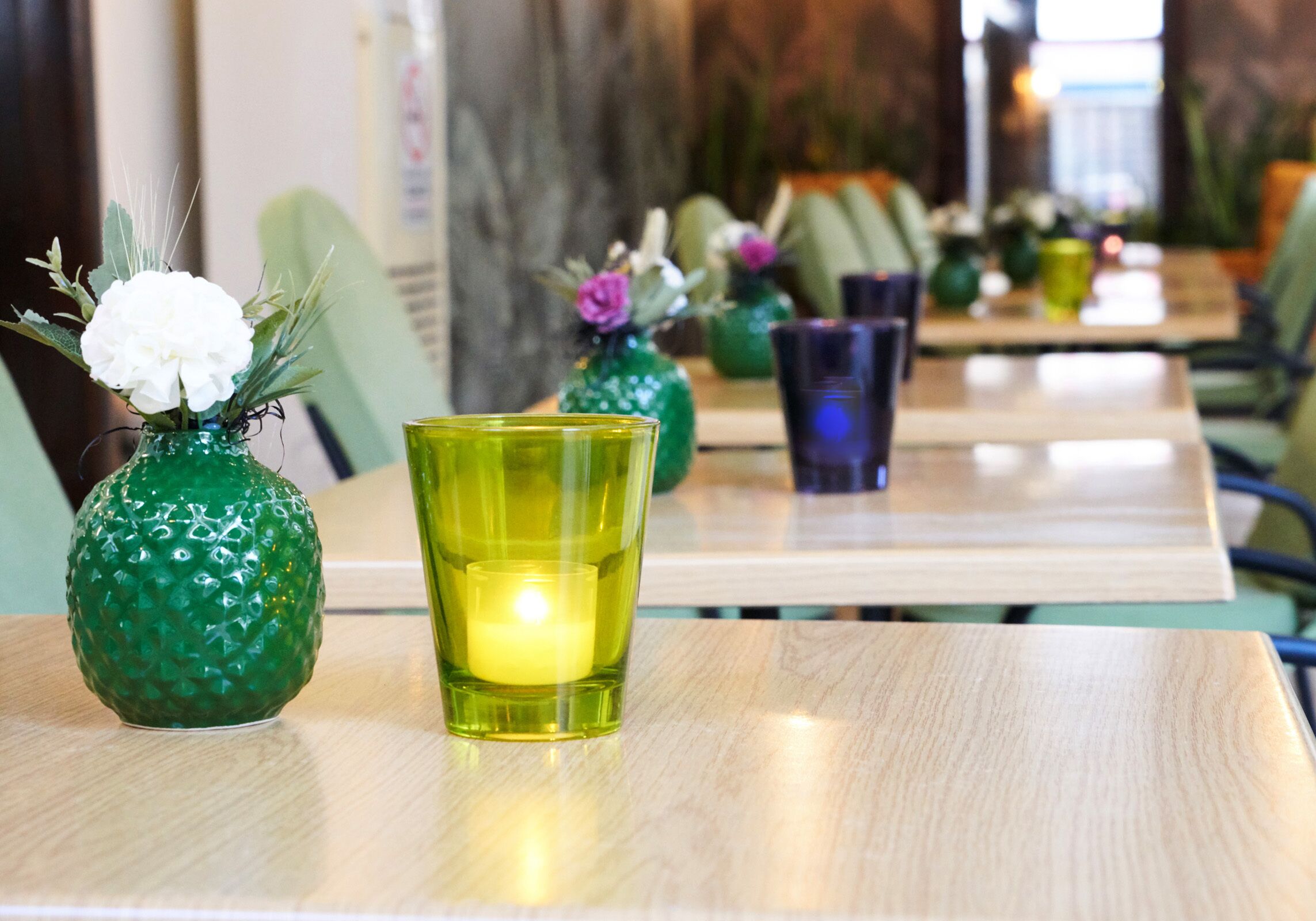 A table with a green textured vase containing a white flower and a lit candle, and a green glass candle holder.
