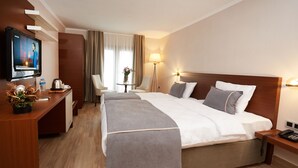 A hotel room with a large bed, a desk with a television, a small table with a vase, and a lamp. - Mira Otel Alsancak (Izmir)