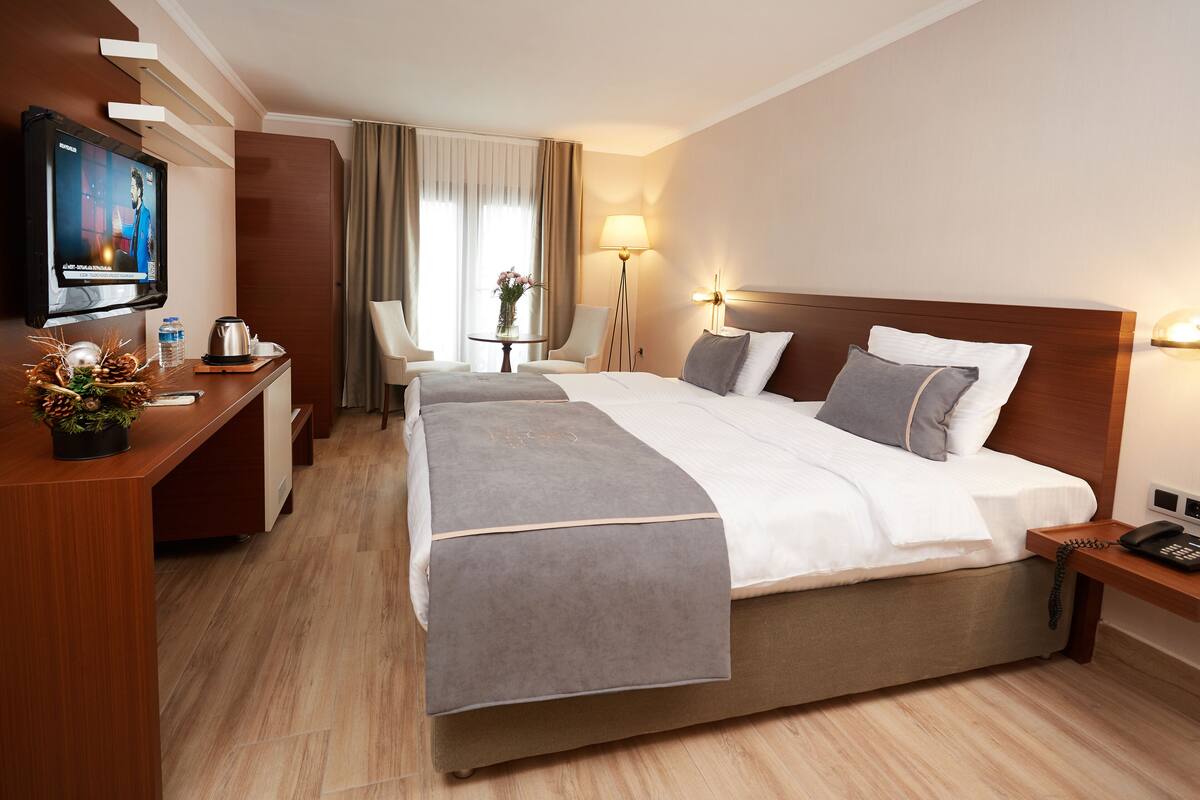 Een hotelkamer met een groot bed, een bureau met een televisie, een klein tafeltje met een vaas en een lamp.