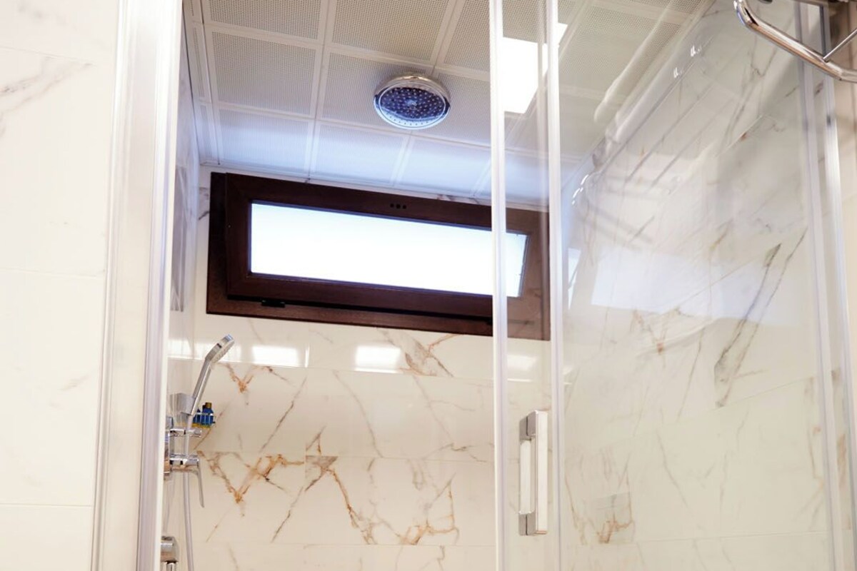 A glass-enclosed shower with a wooden floor and marble walls.