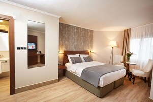 Habitación de hotel con una cama grande, una mesita de noche con lámpara, una silla y un televisor en la pared.