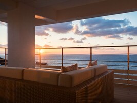 Un balcone con un divano in vimini e cuscini, con vista su un tramonto sull'oceano.