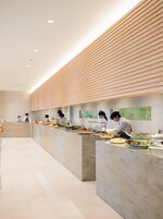 Una cocina moderna con una barra larga, varios chefs preparando alimentos y un diseño limpio y minimalista.