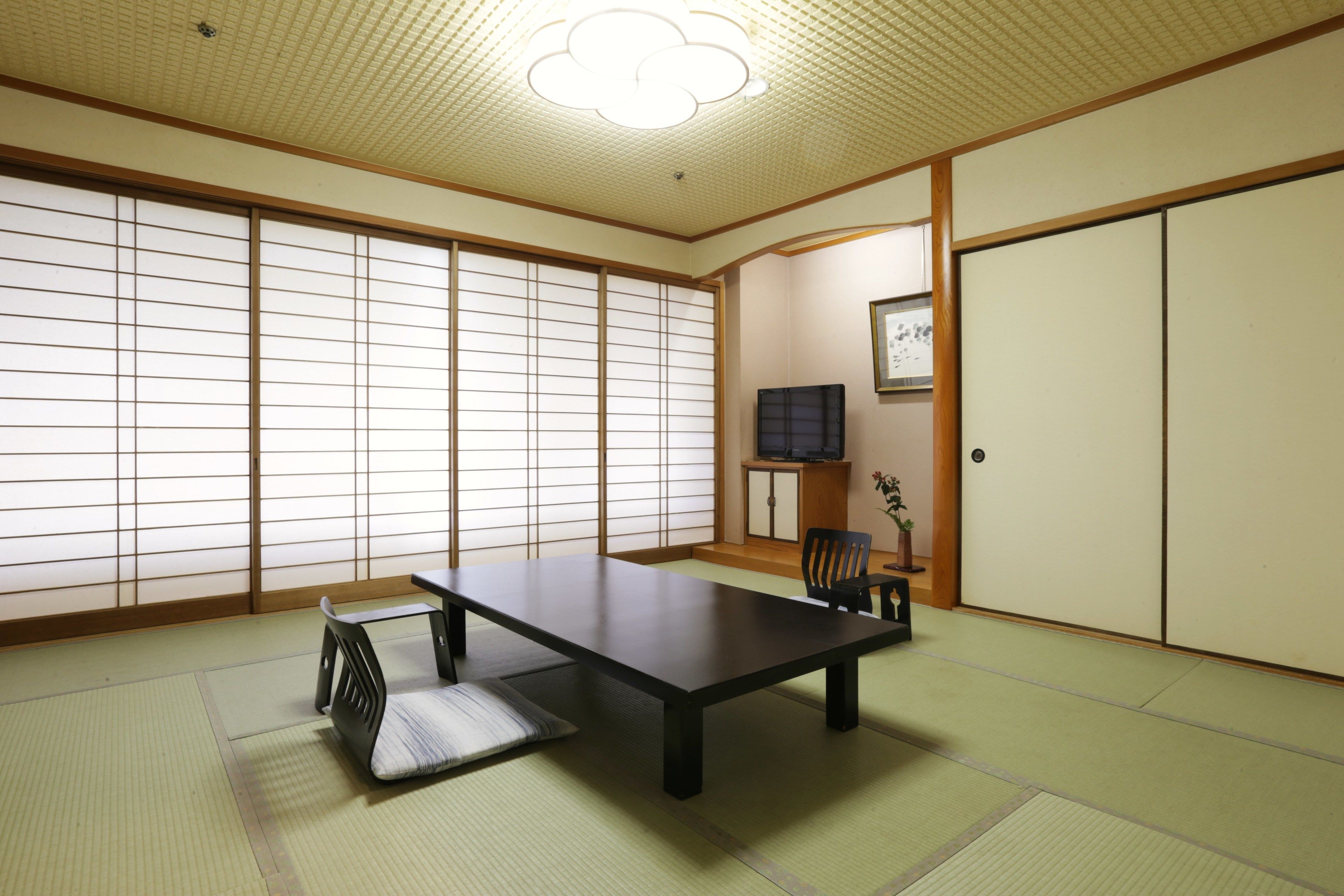 Une pièce de style japonais traditionnel, avec un sol recouvert de tatamis, une table basse, une chaise, des portes coulissantes et un luminaire au plafond.