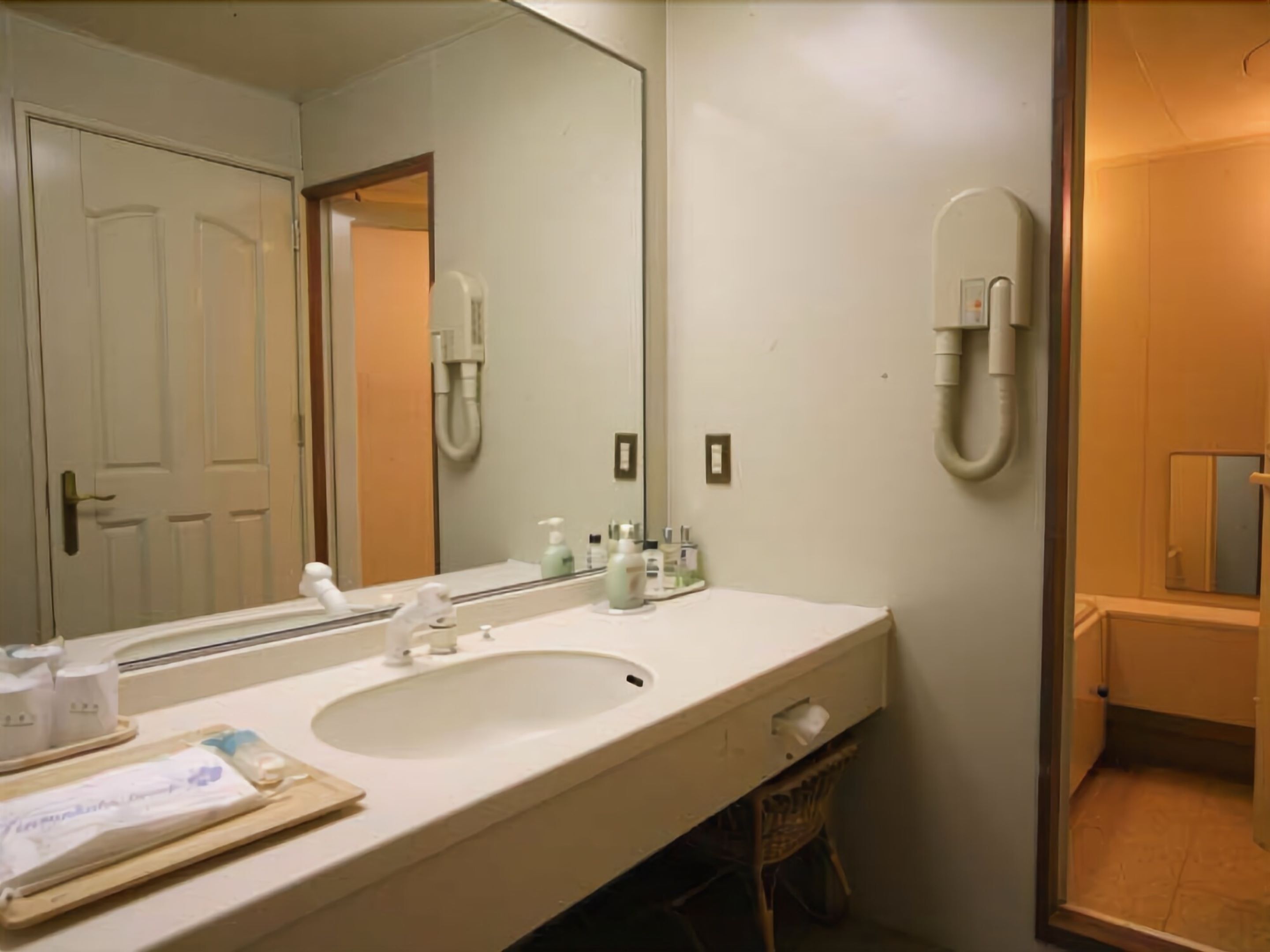 A bathroom with a large mirror, a sink, and a shower. There are toiletries on the sink and a towel rack.