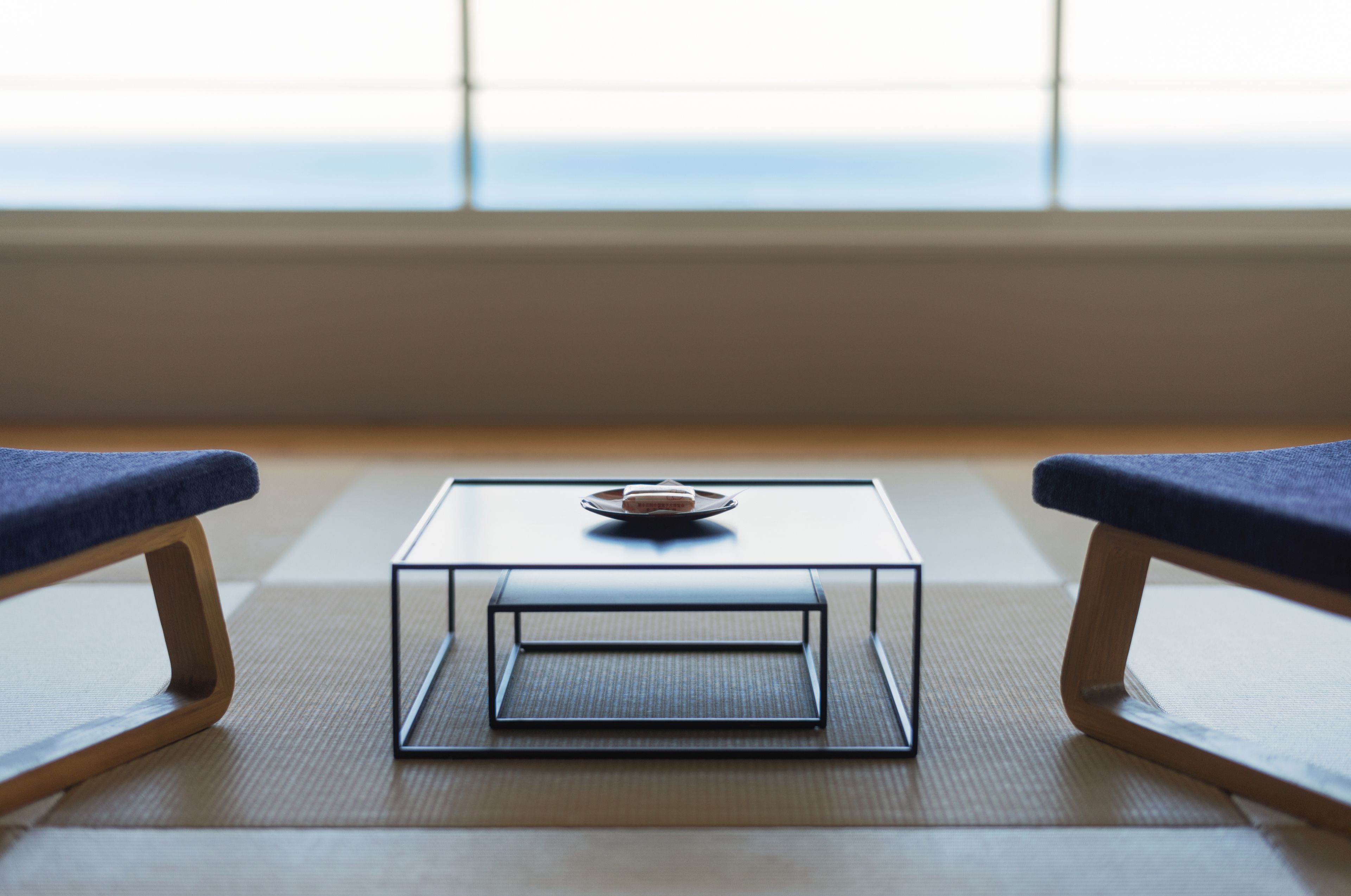 A room with tatami flooring, a low table with a tray, and two blue cushioned chairs.