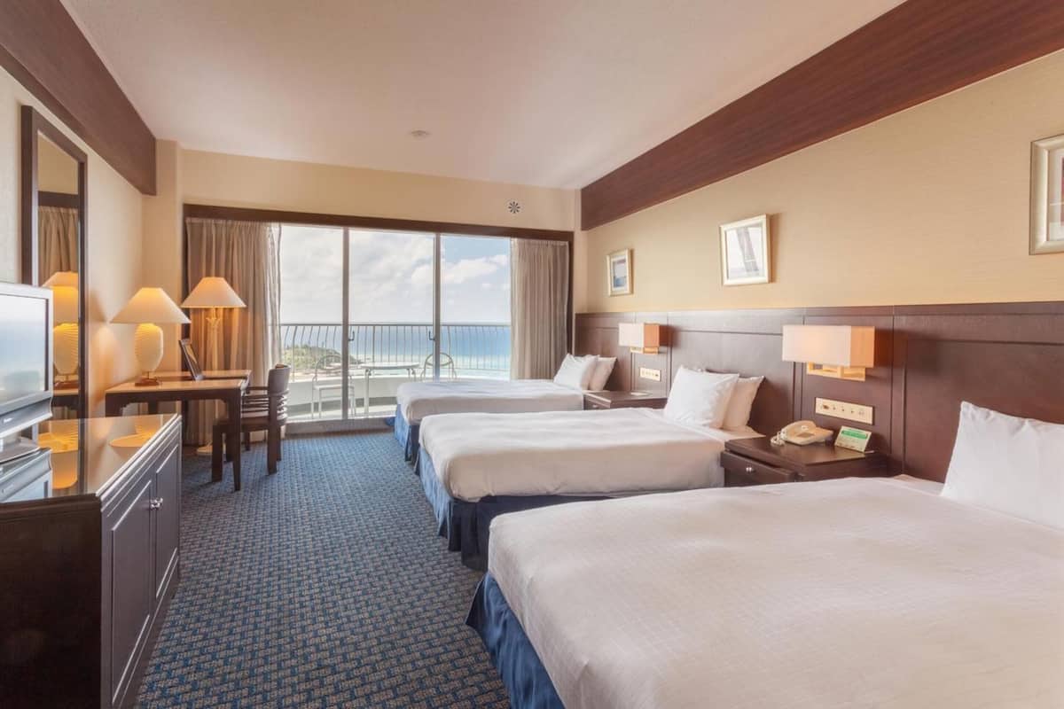 Habitación de hotel con dos camas, un escritorio, una silla, un televisor y un balcón con vistas.
