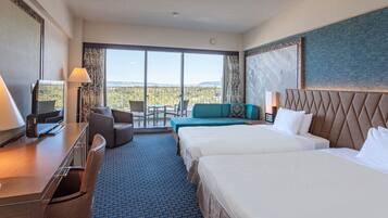 A hotel room with two beds, a desk, a TV, and a balcony with a view.