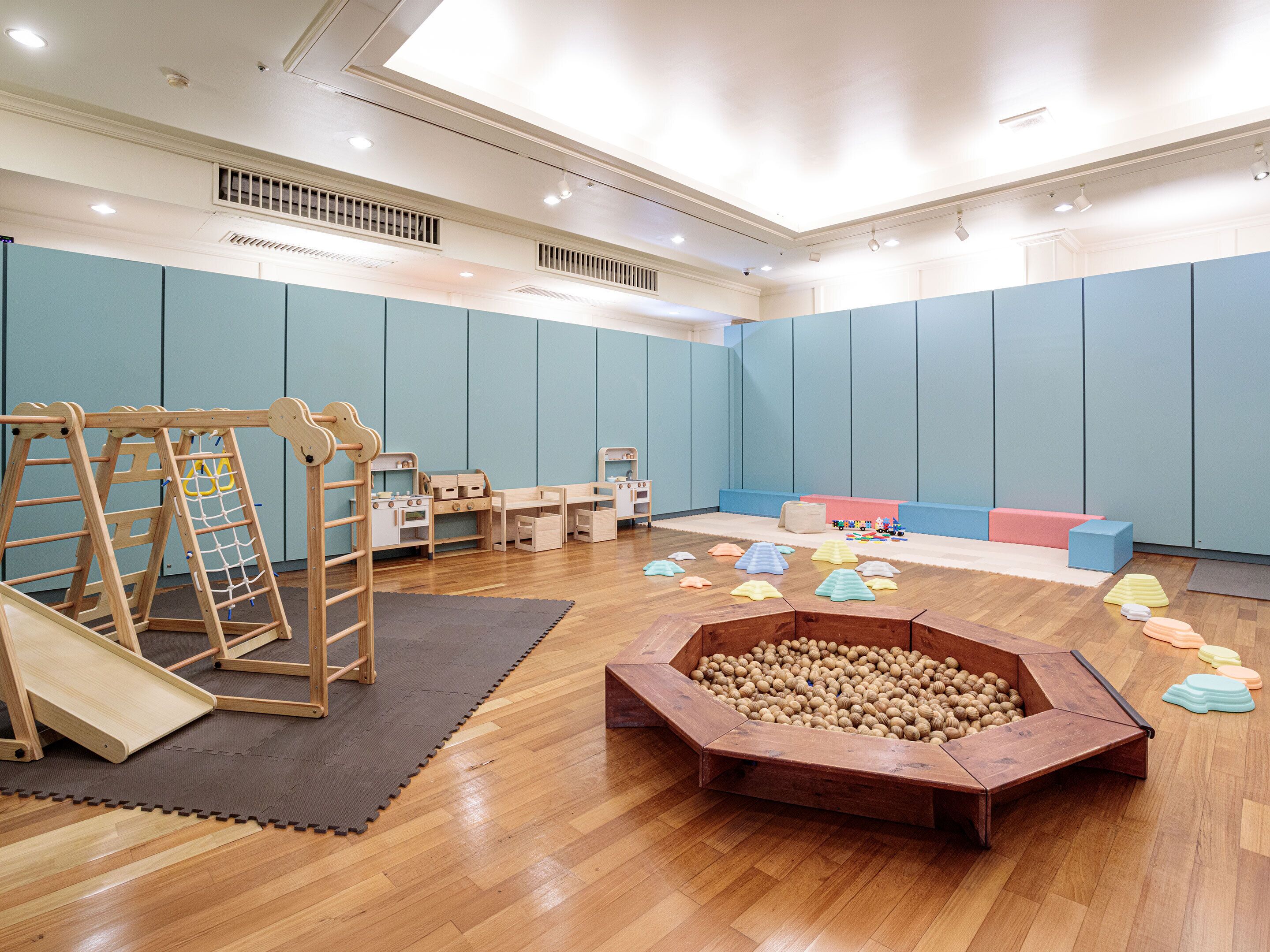 Ein Spielzimmer mit Holzspielgeräten, einer Bällecke und einer Sitzecke.
