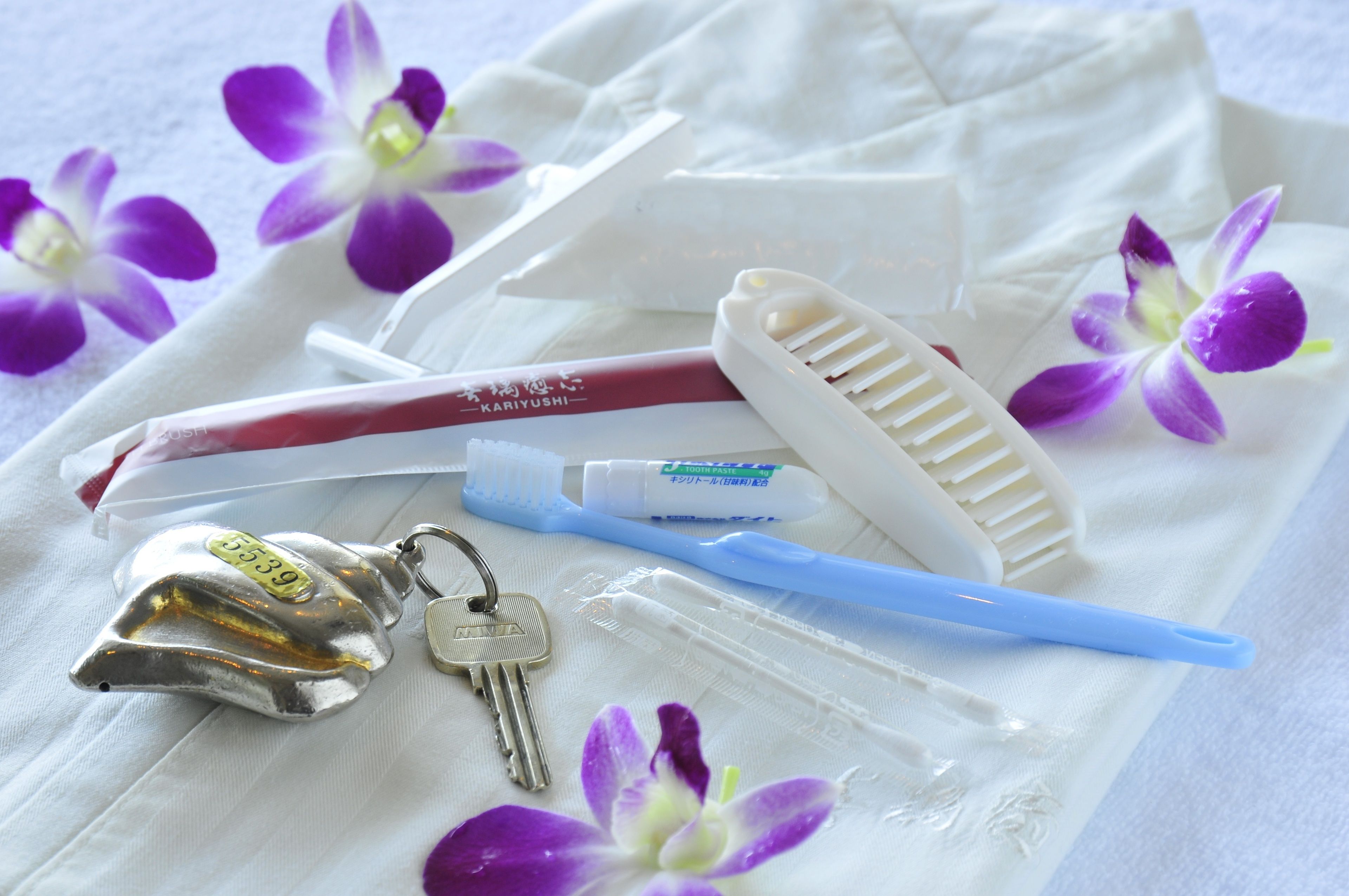A set of personal care items including a comb, toothbrush, and a tube of toothpaste, arranged on a white cloth with purple flowers.