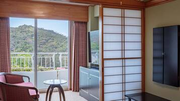 A room with a sliding shoji screen, a TV, a sofa, a small table, and a view of a mountainous landscape.