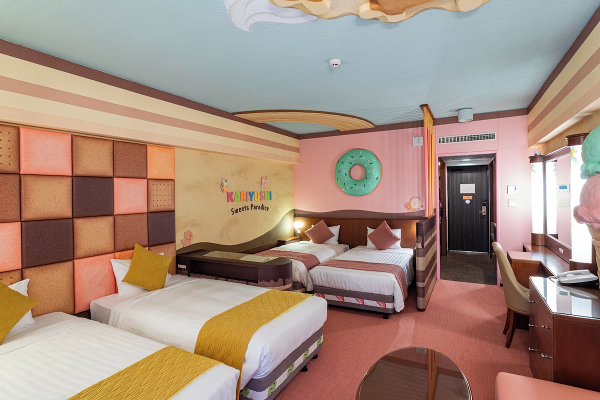 Habitación de hotel con tres camas, un escritorio y una silla.