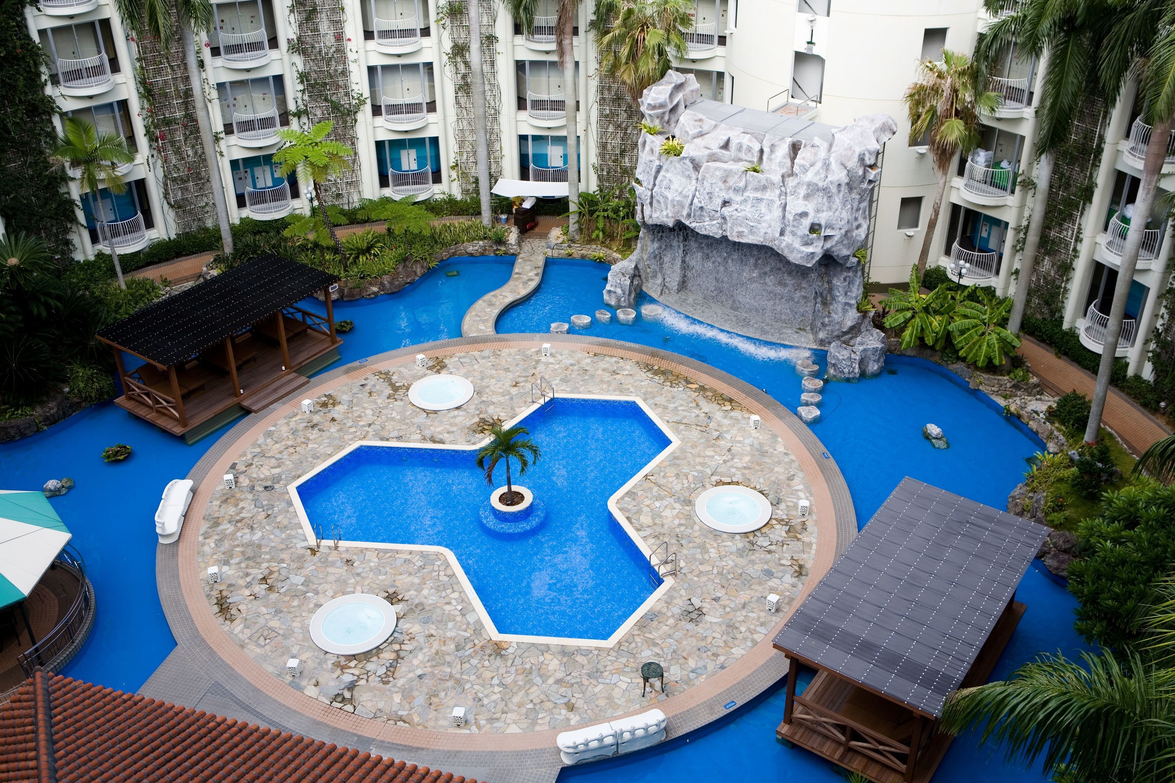 A resort with a central pool, multiple balconies, and lush greenery.