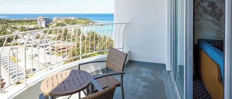 A balcony with a table and two chairs, overlooking a coastal view with buildings and a parking lot.