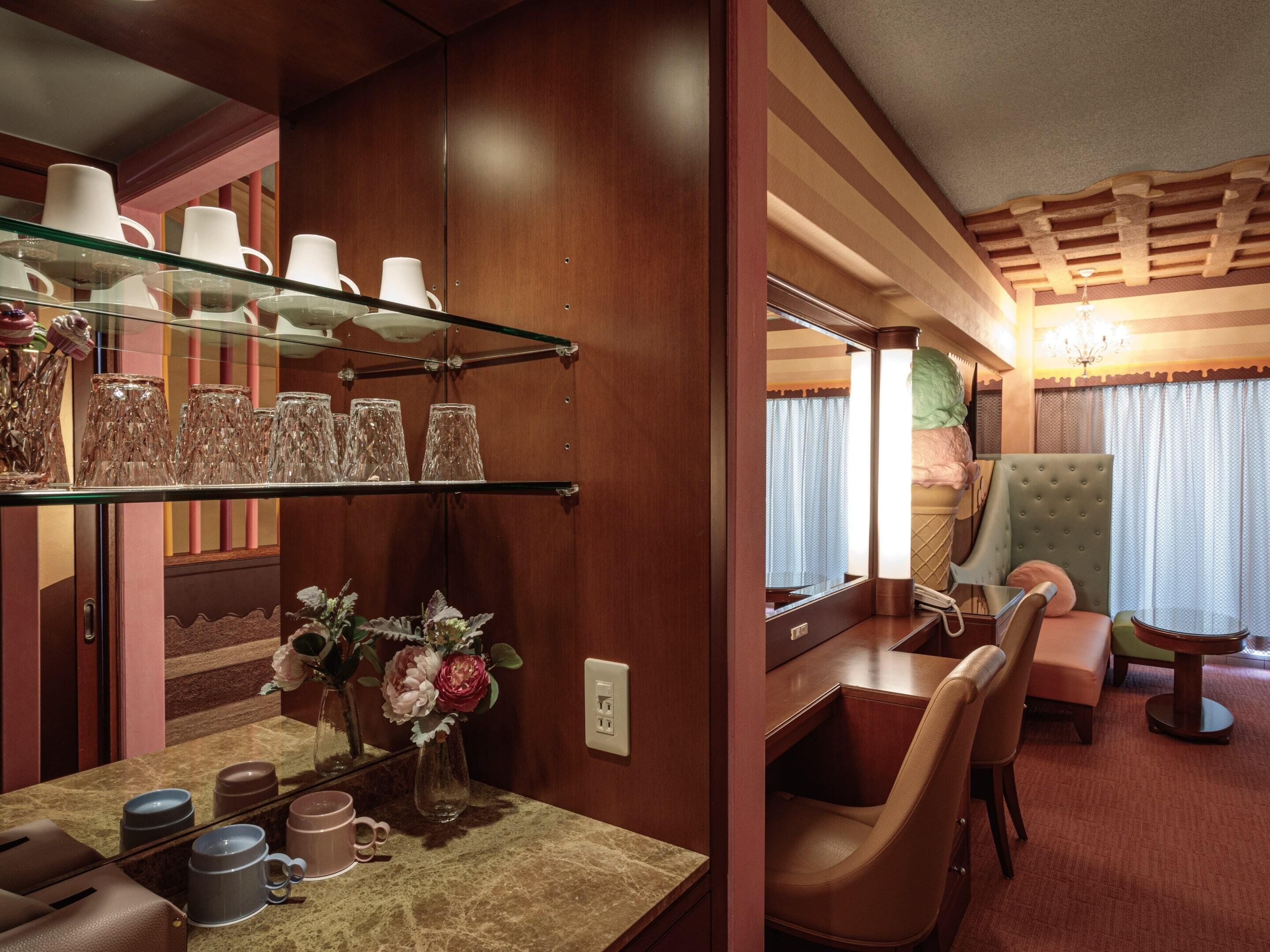 A cozy interior with a wooden vanity, a glass shelf with cups, a mirror, and a plush armchair.