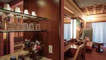 A cozy interior with a wooden vanity, a glass shelf with cups, a mirror, and a plush armchair.