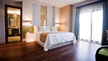 Quarto de hotel com uma cama grande, mesa de cabeceira, espelho e janela com cortinas.