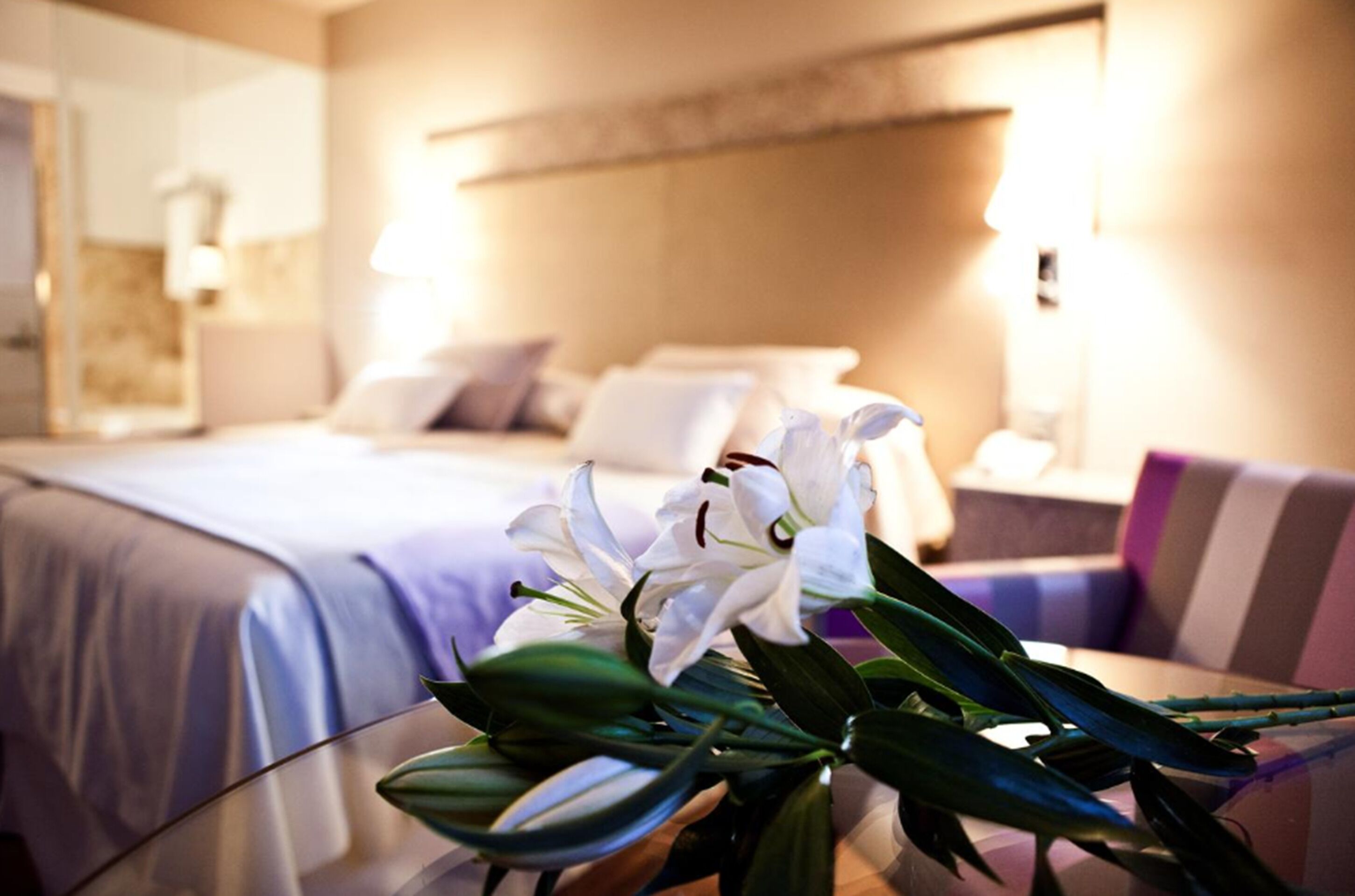 A hotel room with a bed, a glass table with flowers, and a sofa.