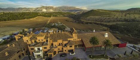 A large, multi-story building with a courtyard, surrounded by agricultural fields and mountains.