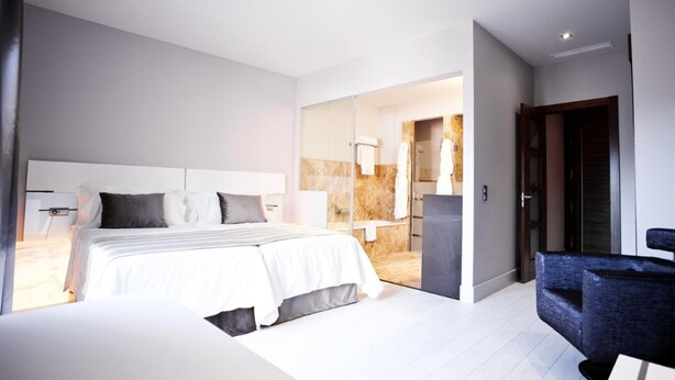 Een moderne hotelkamer met een groot bed, een afzonderlijke zithoek en een badkamer die zichtbaar is door een geopende deur.