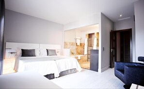 A modern hotel room with a large bed, a separate seating area, and a bathroom visible through an open door. - Hotel & Winery Señorío de Nevada (Villamena)
