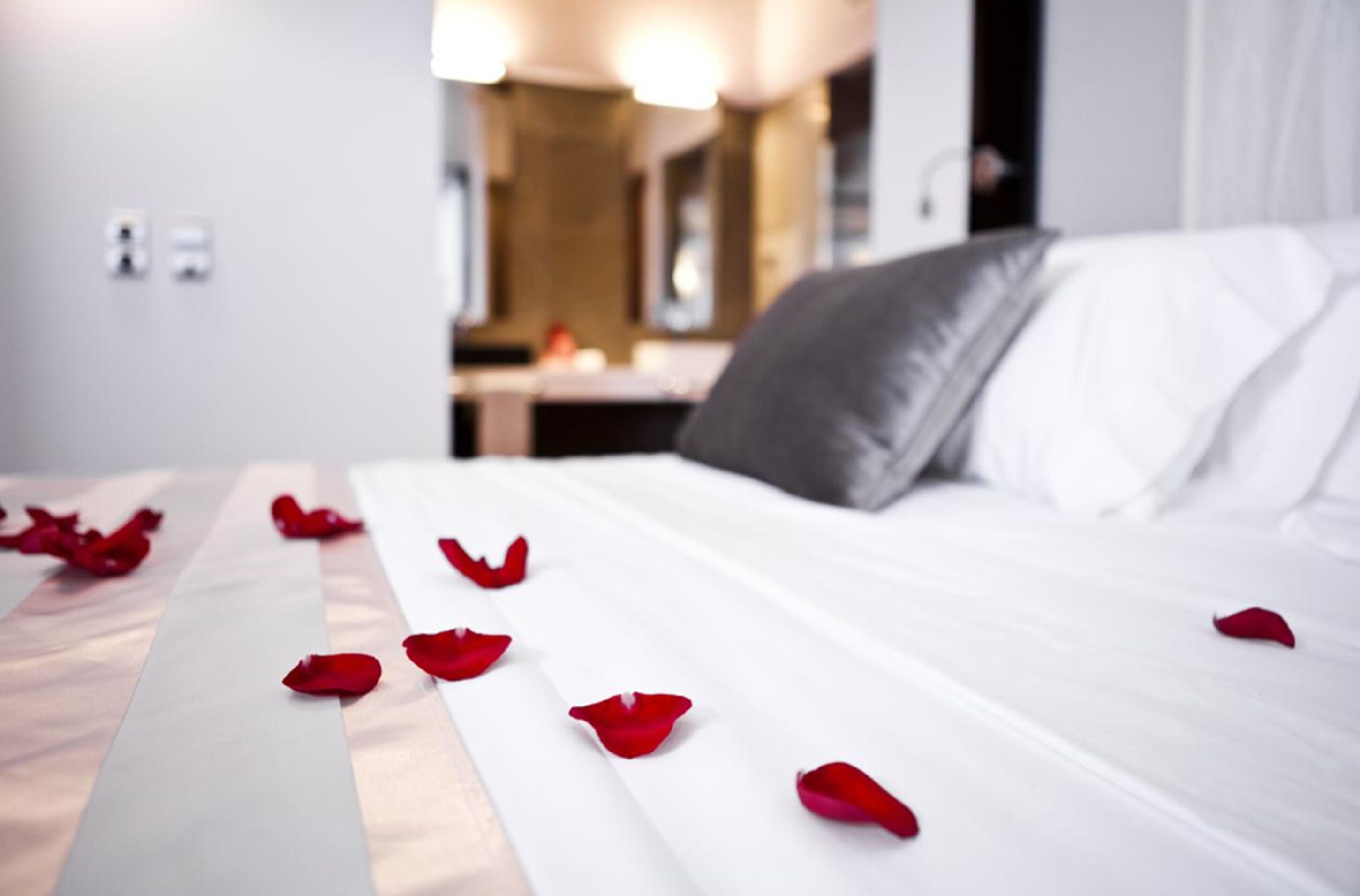 A hotel room with a neatly made bed, a visible bathroom, and a small table with a lamp.