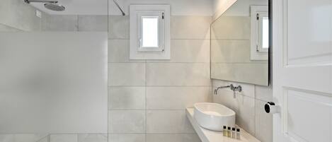 Un baño moderno con cabina de ducha de vidrio, un lavamanos blanco y un espejo grande.