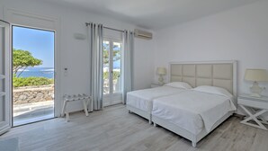 Un dormitorio con una cama grande, un banco y vista al mar a través de un ventanal corredero.