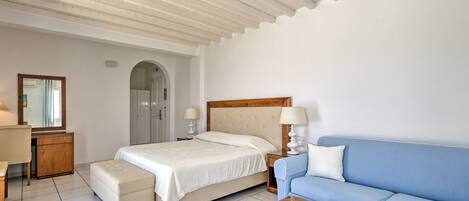 A bedroom with a bed, a blue sofa, a wooden desk, a mirror, and a door.