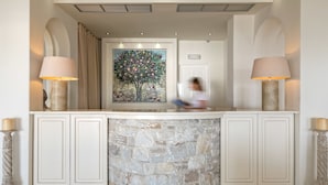 Uma área de recepção com balcão de pedra, duas luminárias, um quadro de uma árvore e uma porta.