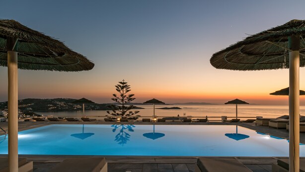Zona junto a la piscina con sillas de descanso, sombrillas y vistas al mar al atardecer.