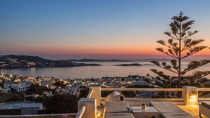 Una terraza con sillones de descanso y vista a un pueblo costero al atardecer.