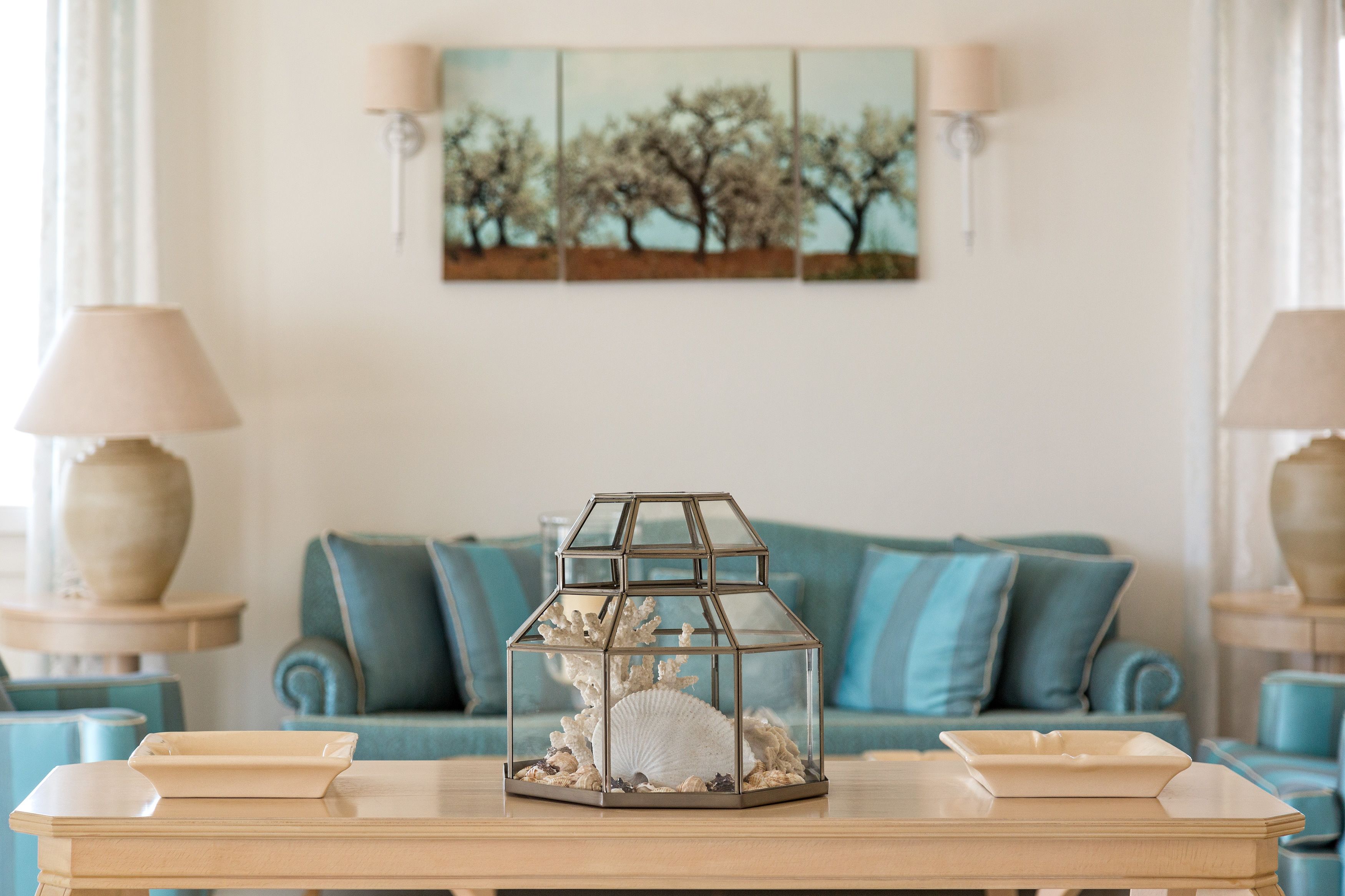 A living room with a glass-top coffee table, a blue sofa, and a wall-mounted painting.