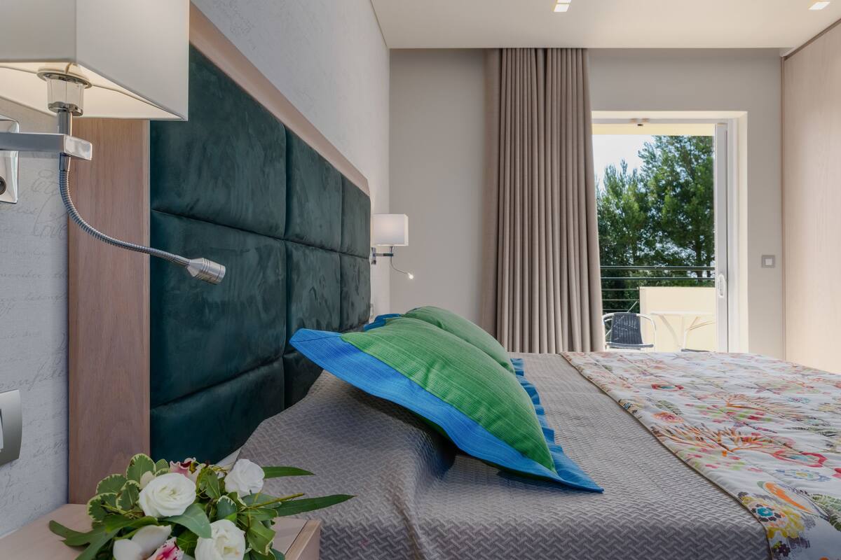 A modern bedroom with a large bed, a headboard, a bedside lamp, and a view of the outdoors.