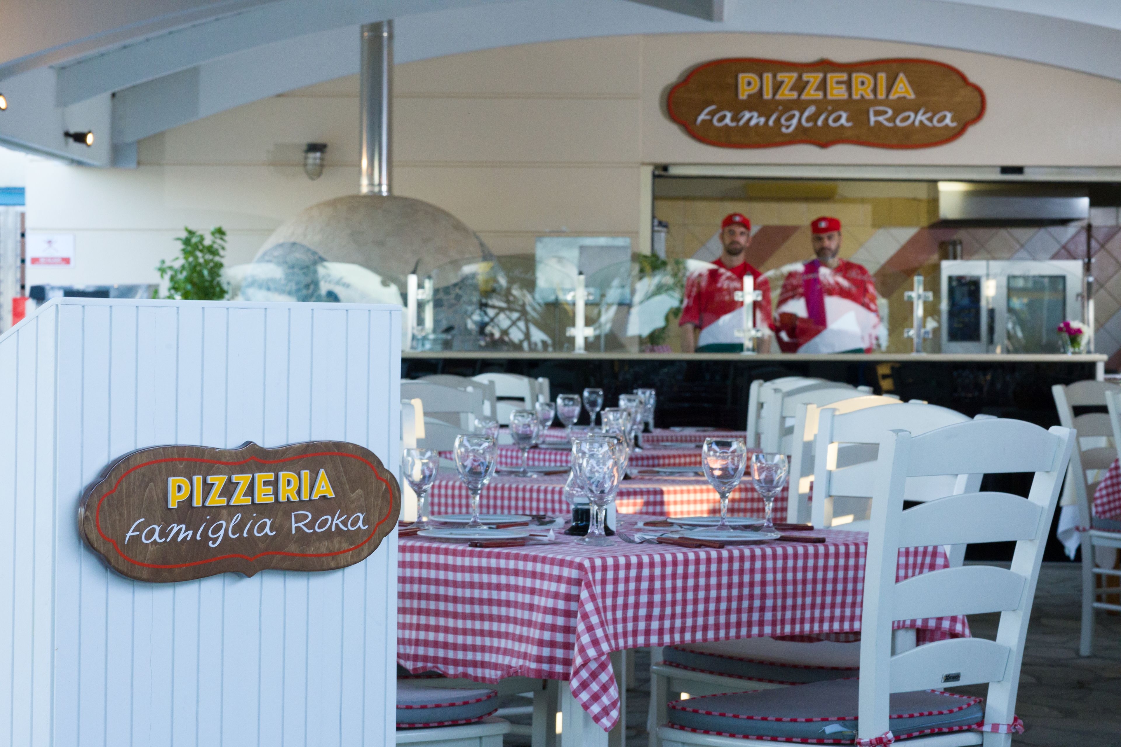 A pizzeria with tables set for dining, a pizza oven, and a sign indicating the name 'Famiglia Roka'.