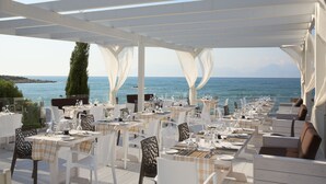 An outdoor dining area with tables and chairs, overlooking a body of water.