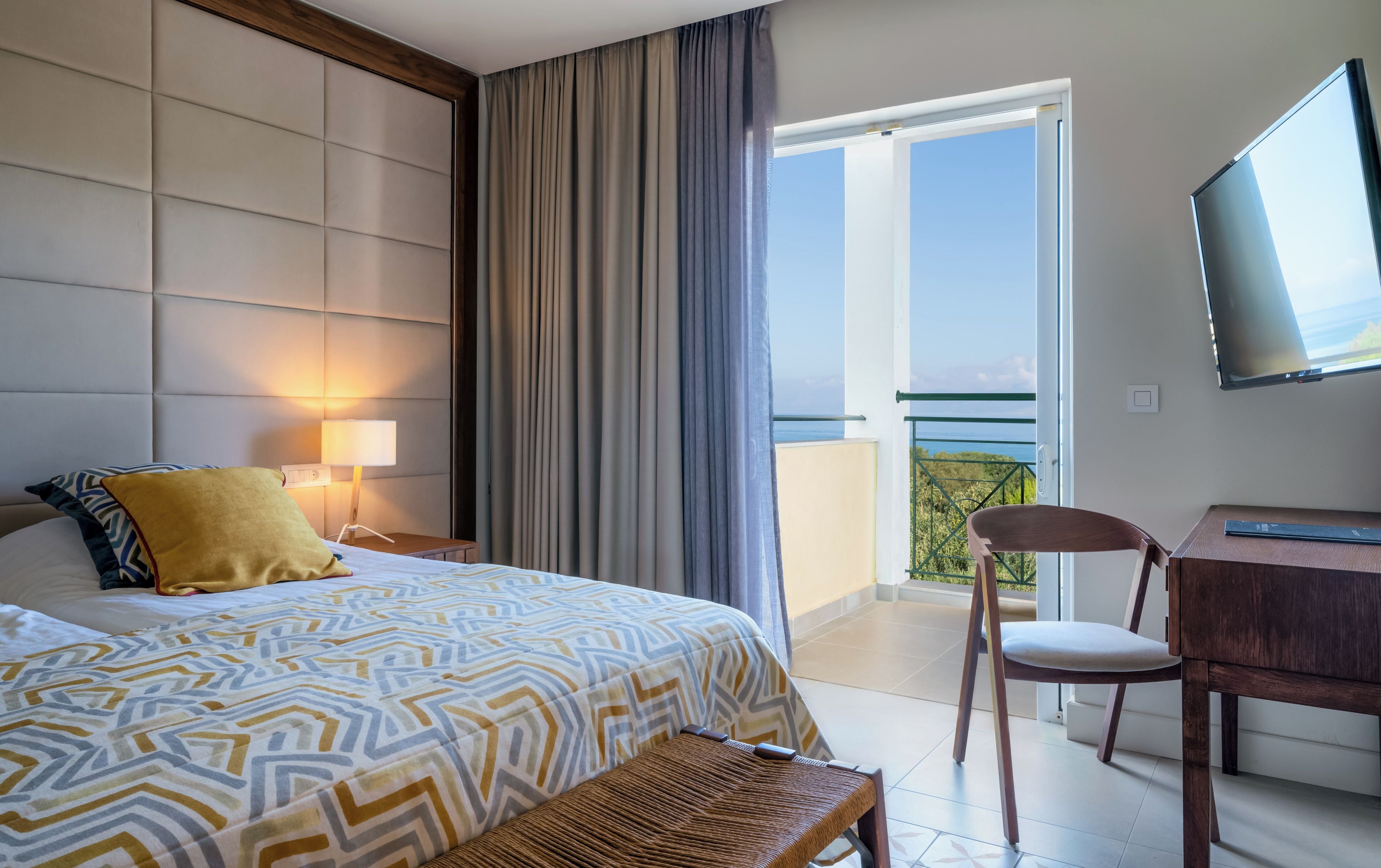A hotel room with a bed, a desk, a chair, a TV, and a balcony with a view.