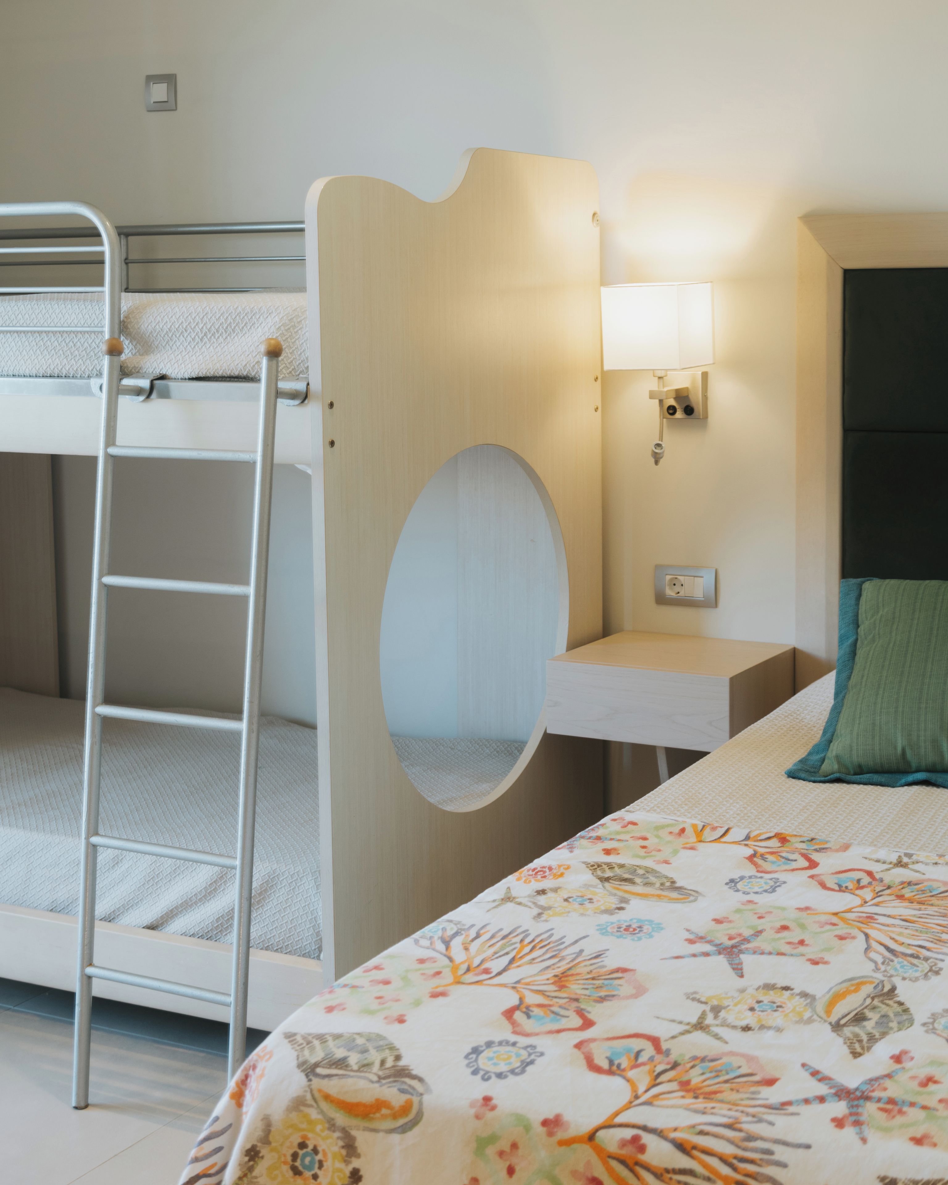 A bunk bed with a ladder, a bedside table with a lamp, and a bed with a floral-patterned bedspread.