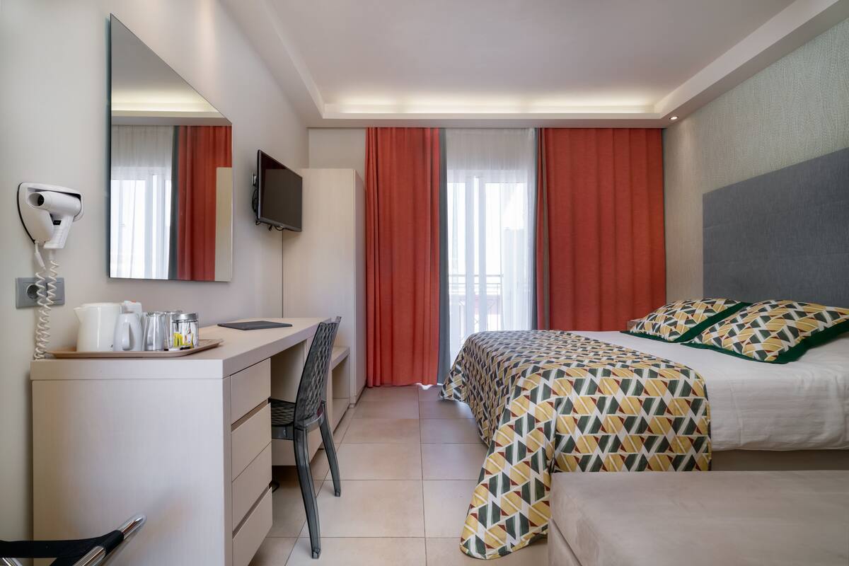 A hotel room with a bed, a desk, a chair, a TV, and a mirror.